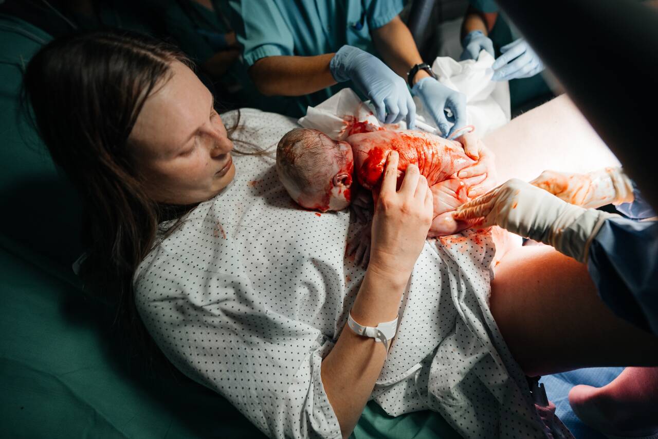 Mãe segurando bebê recém-nascido em sala de parto.