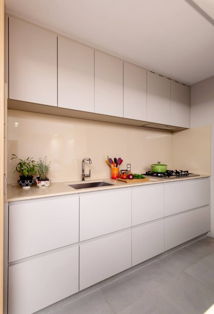Uma cozinha moderna e minimalista em tons neutros. Armários e bancadas cinza-claro, com um backsplash creme. Um fogão e pia de aço inoxidável são visíveis, junto com vasos de plantas e utensílios de cozinha coloridos.