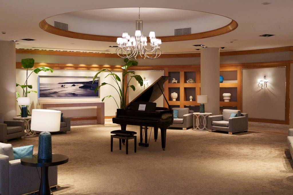 Lobby interior de um hotel, com um piano ao centro e sofas ao redor