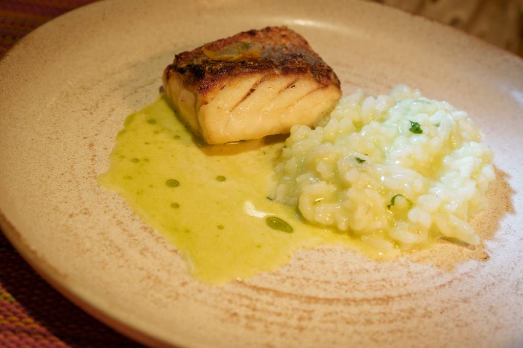 Prato branco com uma posta de peixe, arroz e molho para acompanhar