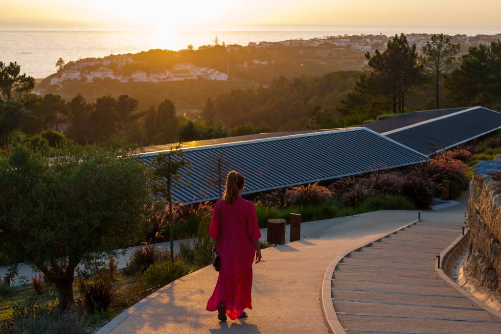 _1Nc8796 Mulher de vestido cor de rosa caminha pelo hotel ao por do sol