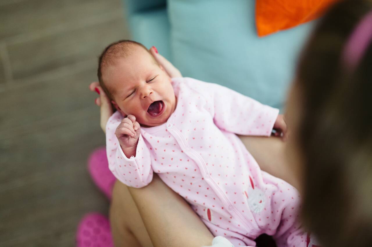 Bebê de macacão rosa bocejando nos braços de uma pessoa