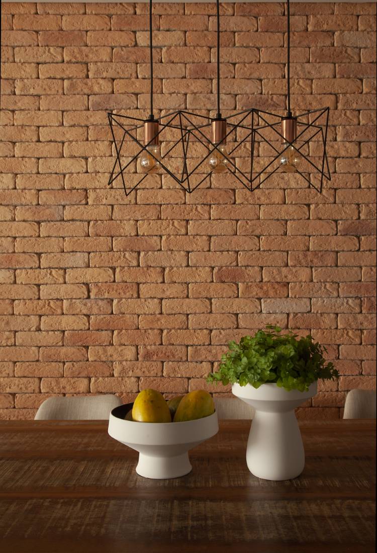 Cozinha-Rustica-Moderna-4 Sala de jantar com parede de tijolinhos aparentes e uma luminária pendente de metal com design geométrico. Sobre a mesa de madeira rústica, um vaso branco com plantas e uma fruteira com limões.