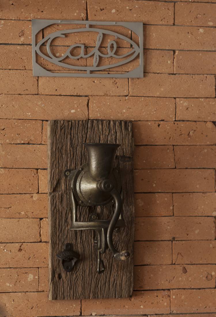 Cozinha-Rustica-Moderna-6 Na parede de tijolinhos de uma cozinha rústica moderna, um moedor de café antigo de ferro fundido está montado em uma tábua de madeira rústica, com um abridor de garrafas ao lado. Acima, um letreiro "Café" de metal.