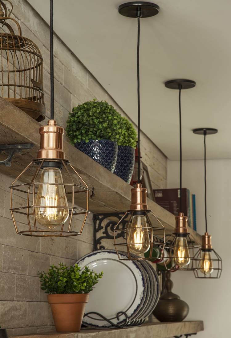 Cozinha-Rustica-Moderna-7 Vista próxima de prateleiras de madeira em uma cozinha rústica moderna. Destaque para as luminárias pendentes em tom cobre com design industrial, iluminando pratos decorativos e pequenos vasos de plantas.