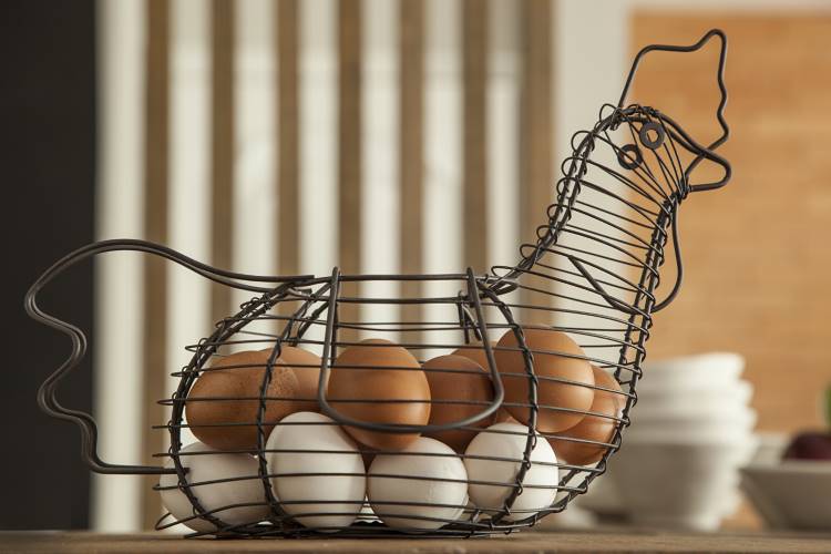 Cozinha-Rustica-Moderna-1 Nesta cozinha rústica moderna, uma cesta de ovos em forma de galinha, feita de metal preto, está cheia de ovos brancos e marrons. A cesta repousa sobre uma mesa de madeira.