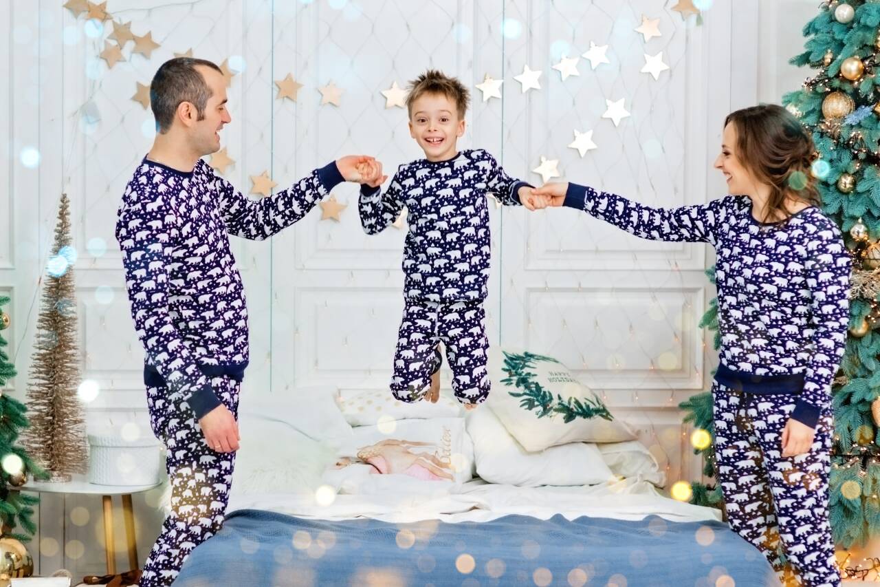 Família em pijamas festivos pulando juntos na cama.