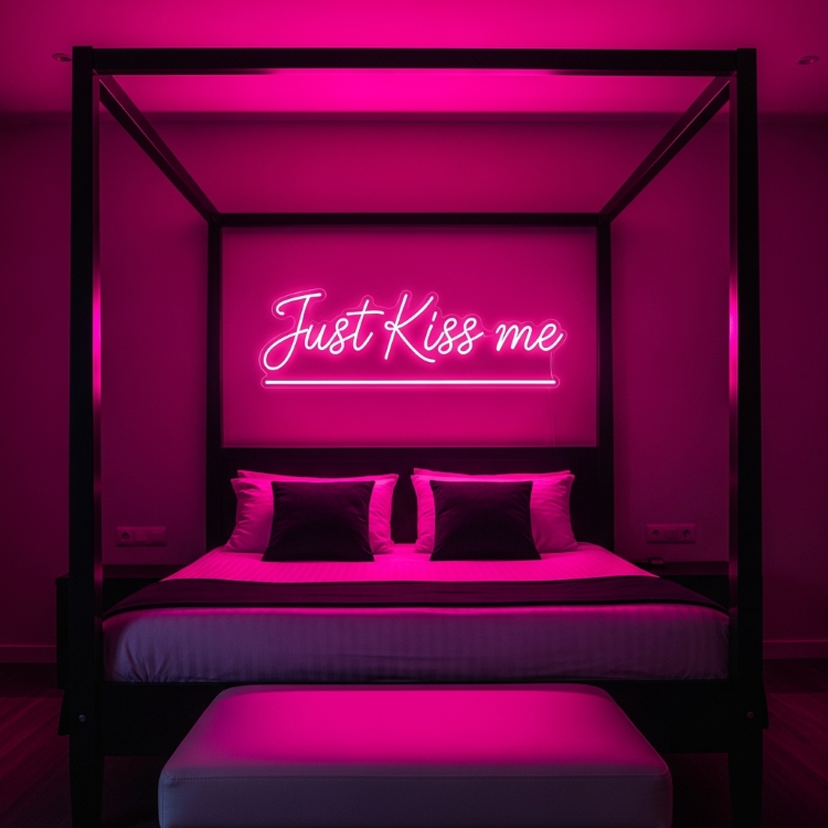 Uma cama de dossel preta. Na cabeceira, a parede é iluminada por um letreiro de neon rosa que diz "Just Kiss me". A cama tem lençóis brancos e travesseiros escuros. Um banco estofado está aos pés da cama.