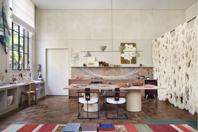 Loft com paredes e móveis em tons de off white com piso de taco de madeira e tapete colorido