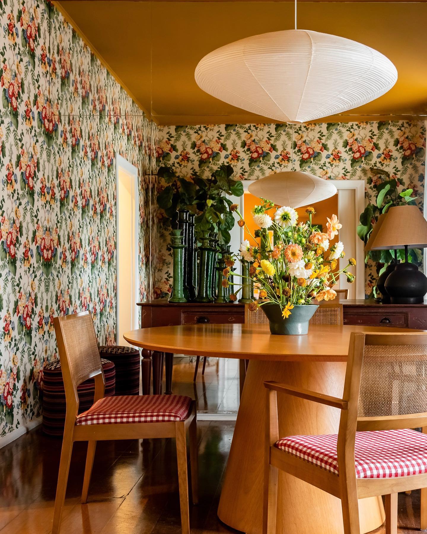 sala de jantar com papel de parede floral, cadeiras estampadas e luminária vintage.