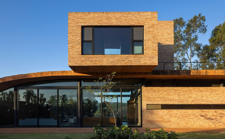 Parte traseira da Passive House com sol batendo na fachada em tijolo aparente e materiais naturais.