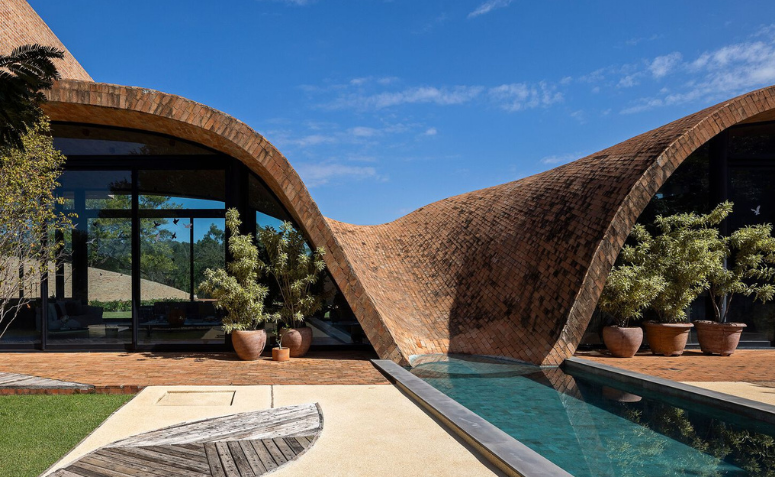Vista externa da Passive House destacando a curva em tijolo aparente integrada à área da piscina.