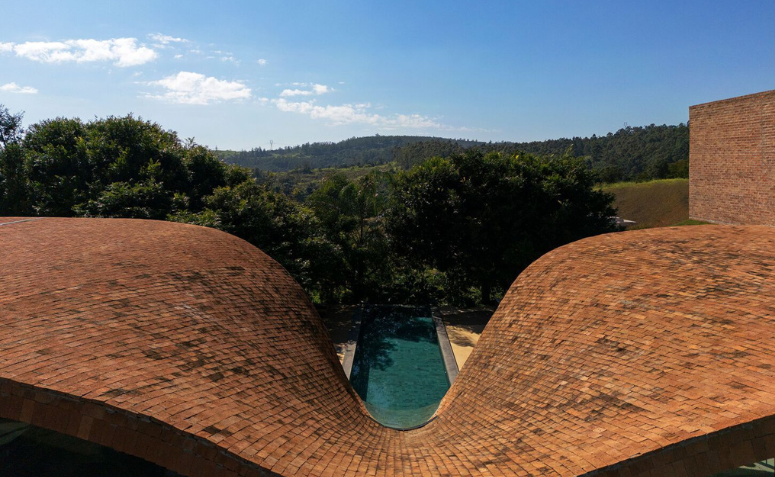 Vista aérea da cobertura curva da Passive House conduzindo água da chuva para a piscina, com integração à paisagem natural