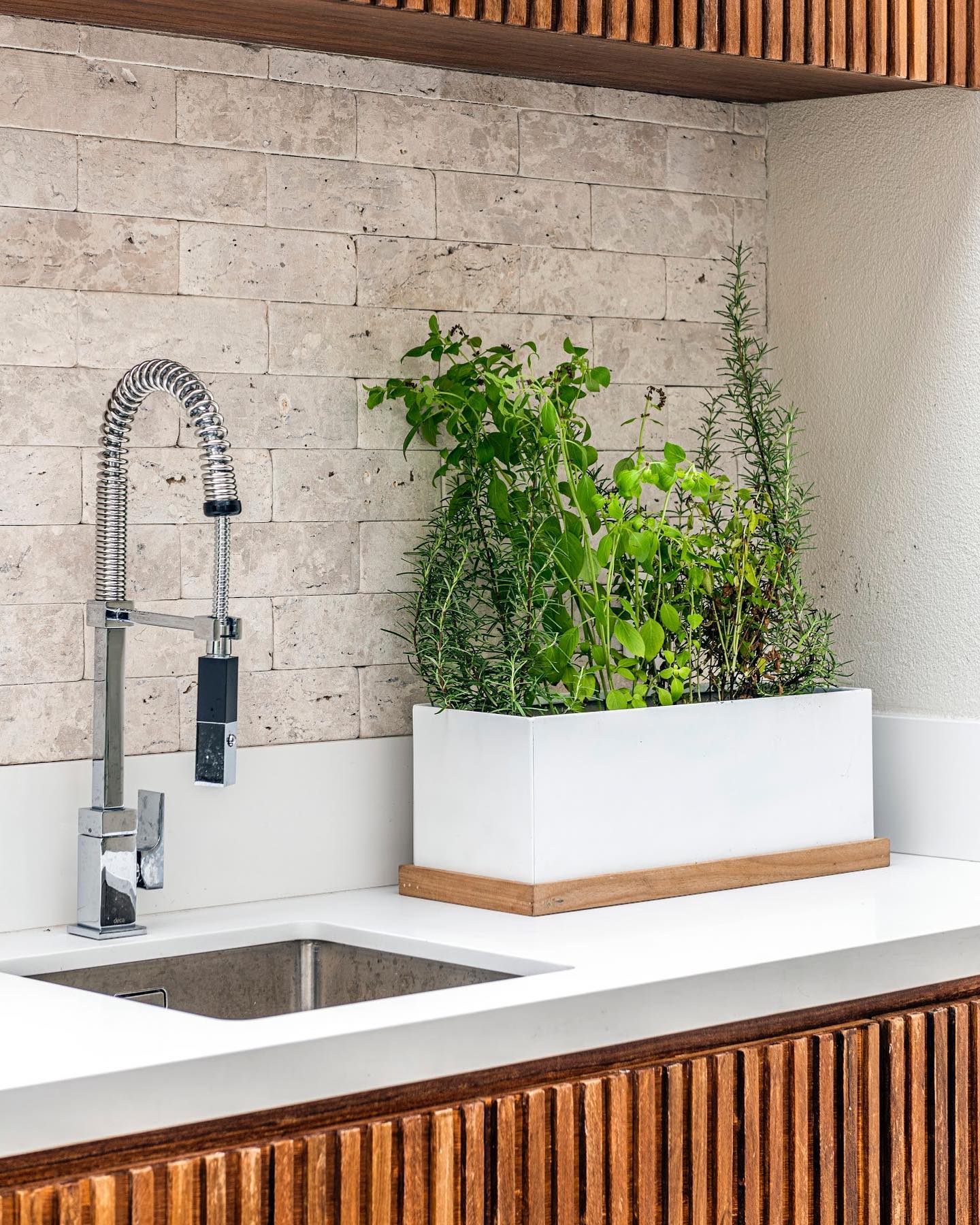 bancada de varanda com floreira de temperos frescos ao lado da pia.