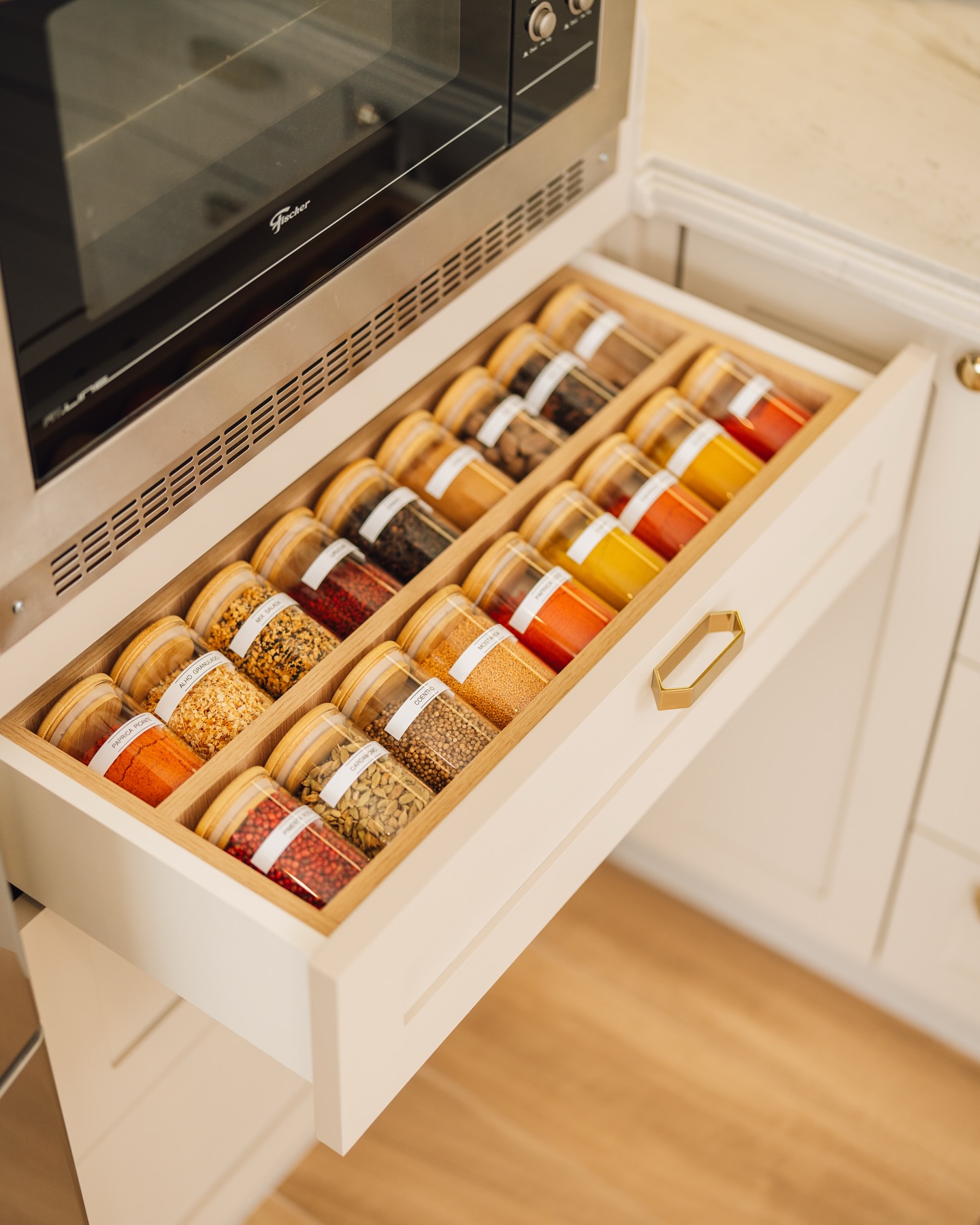 Gaveta de cozinha com potes de temperos organizados em fileiras e rótulos voltados para cima, facilitando o acesso e mantendo o visual limpo.