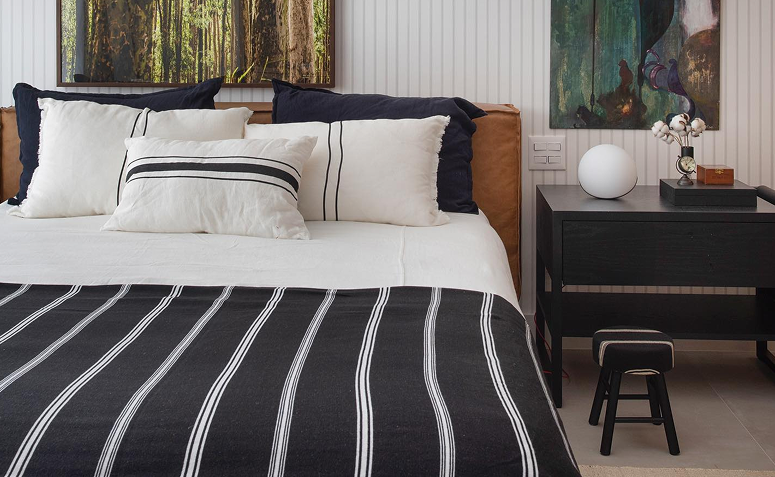 Cama arrumada com colcha listrada preta e branca e travesseiros brancos, mostrando organização simples e rápida