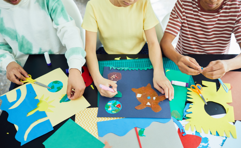 três crianças fazendo artesanato para fazer com as crianças, criando uma colagem com papéis coloridos