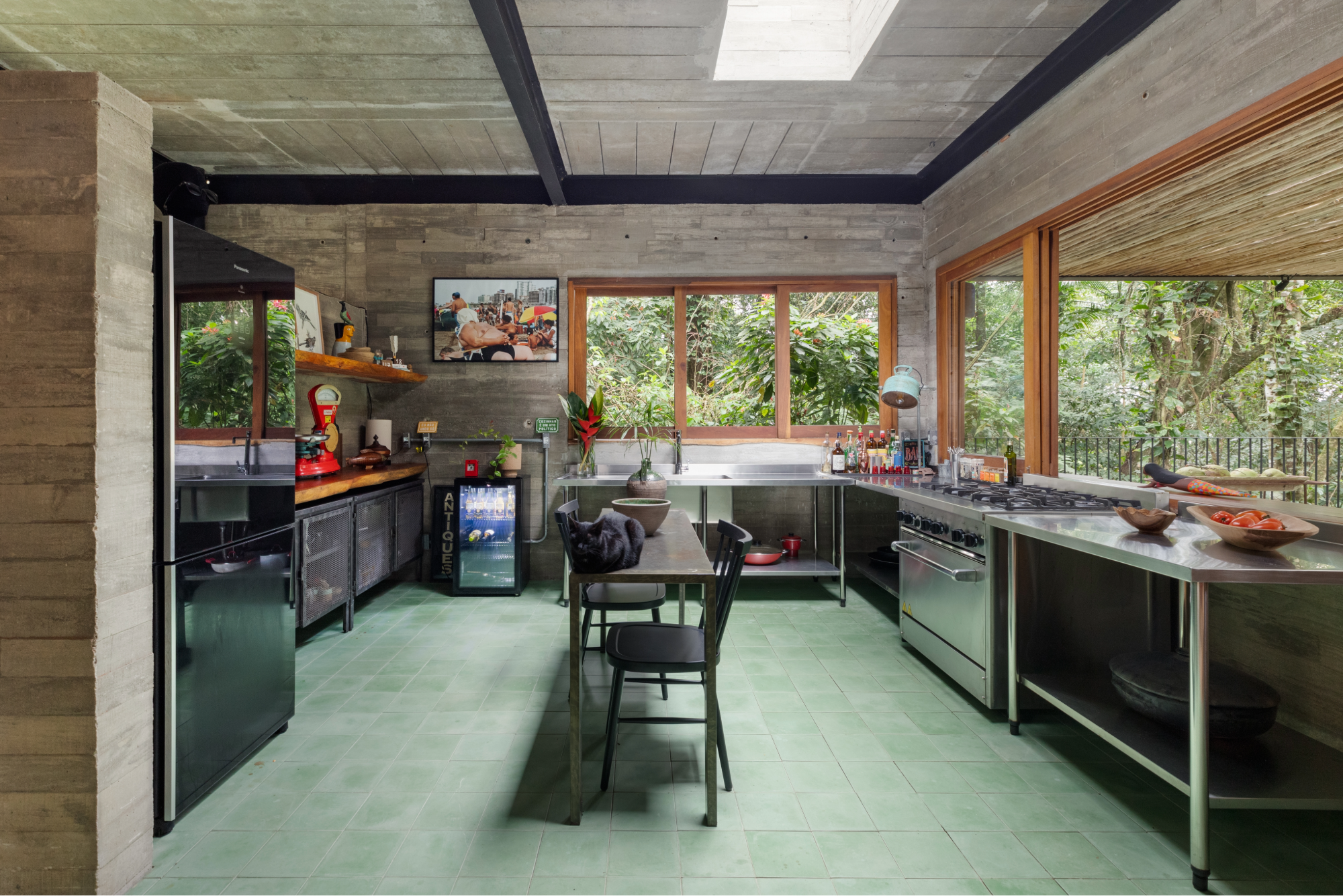 Cozinha com módulos industriais de inox, claraboia e integração total com sala e varanda.