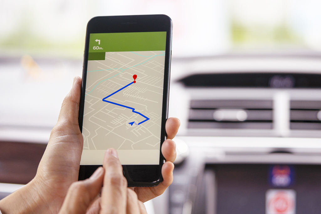 Foto de uma pessoa dentro do carro segurando um celular com GPS.