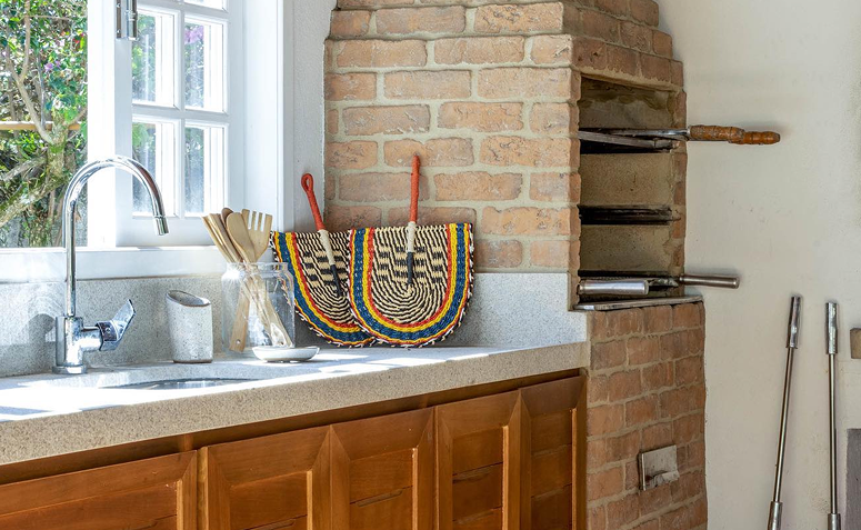 Churrasqueira de tijolinhos com grelhas e espetos, ao lado da pia, mostrando o uso no dia a dia e a importância da limpeza