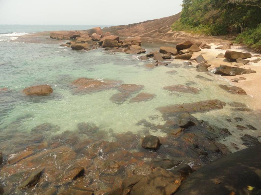 Pedras em uma praia, com águas verdes e cristalinas.