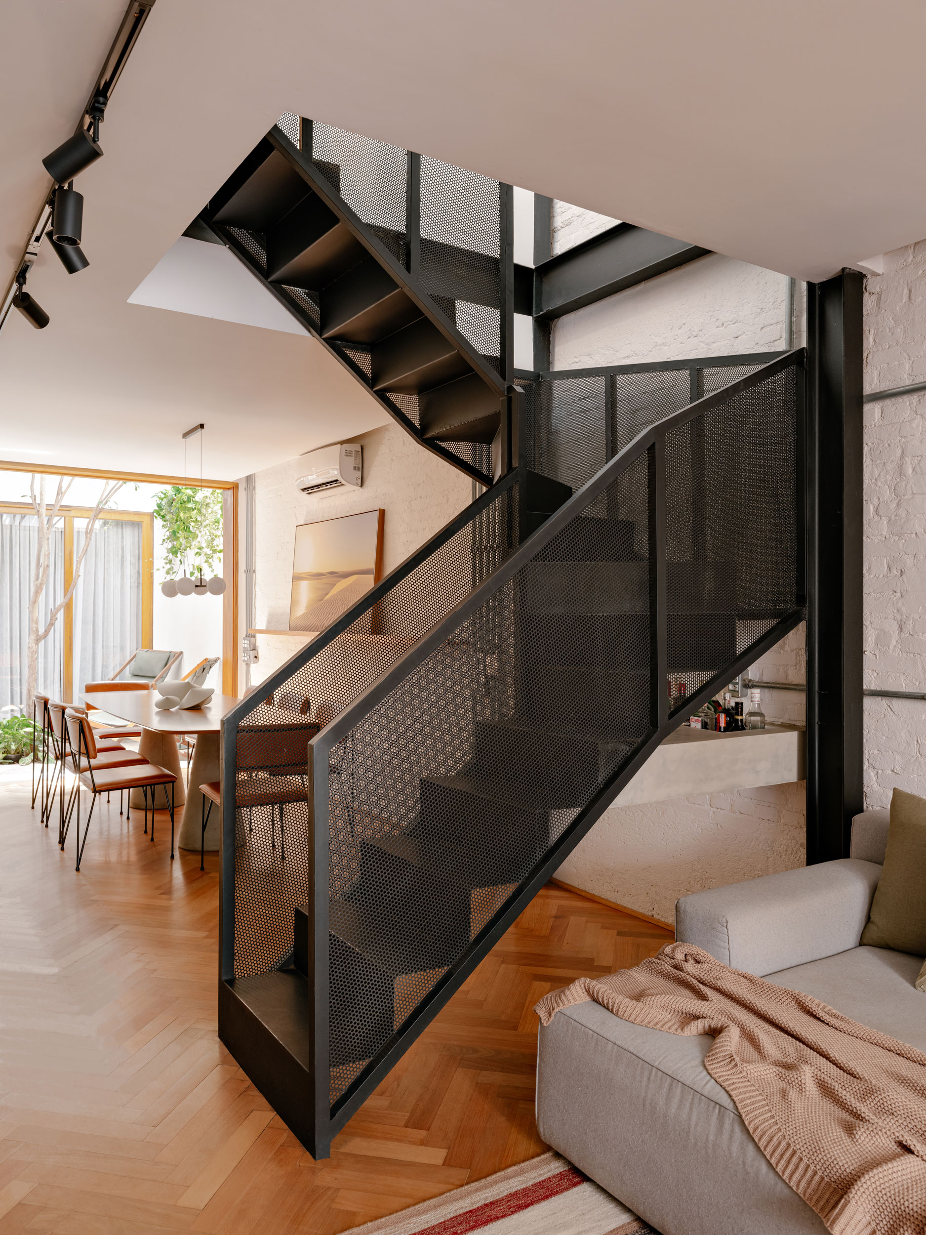 Escada metálica com guarda-corpo perfurado na Casa MA, com bar em concreto sob o vão e iluminação natural zenital.