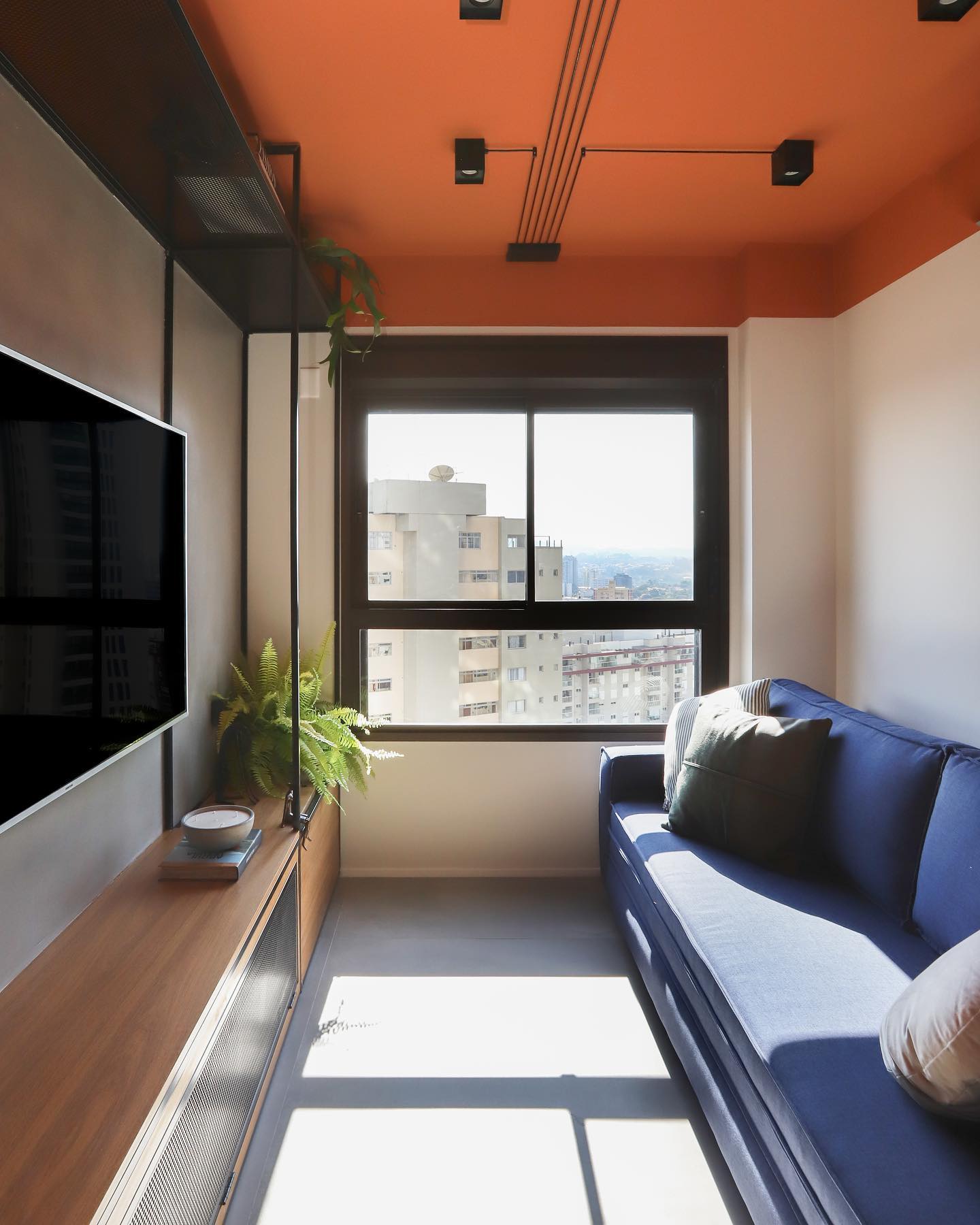 Teto com moldura pintado em laranja, com a cor descendo alguns centímetros pelas paredes, destacando a área da janela e criando um efeito acolhedor na sala compacta.