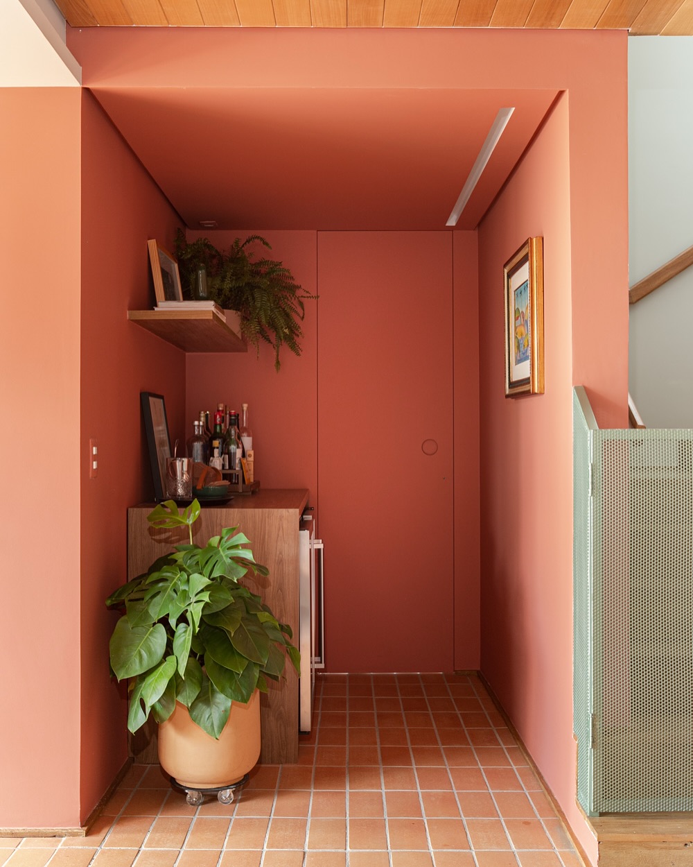 Ambiente com efeito de teto caixa, onde teto, paredes e porta recebem a mesma cor terracota, criando um espaço contínuo e acolhedor.