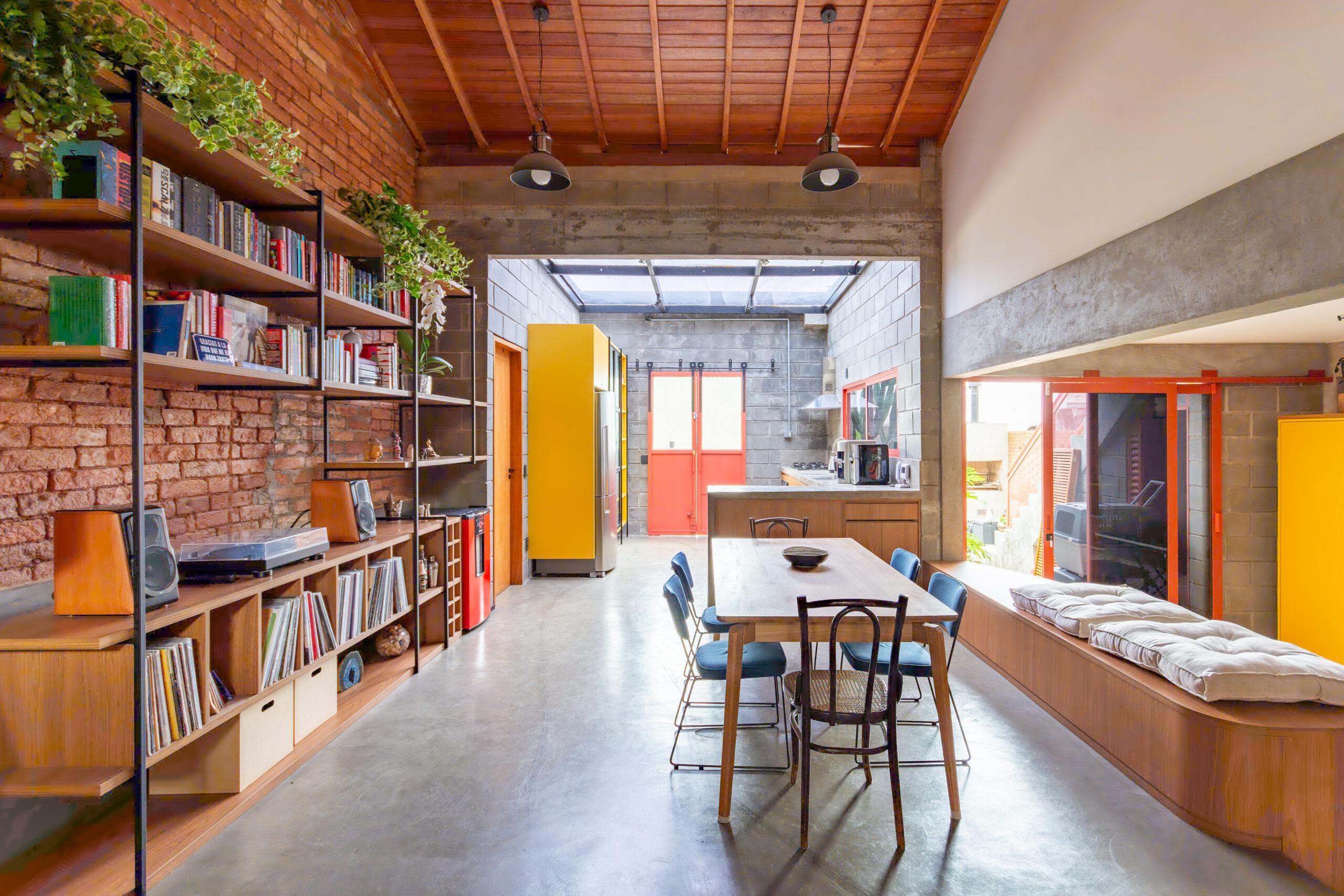 Sala integrada com cozinha, estante em marcenaria e serralheria e mezanino ao fundo