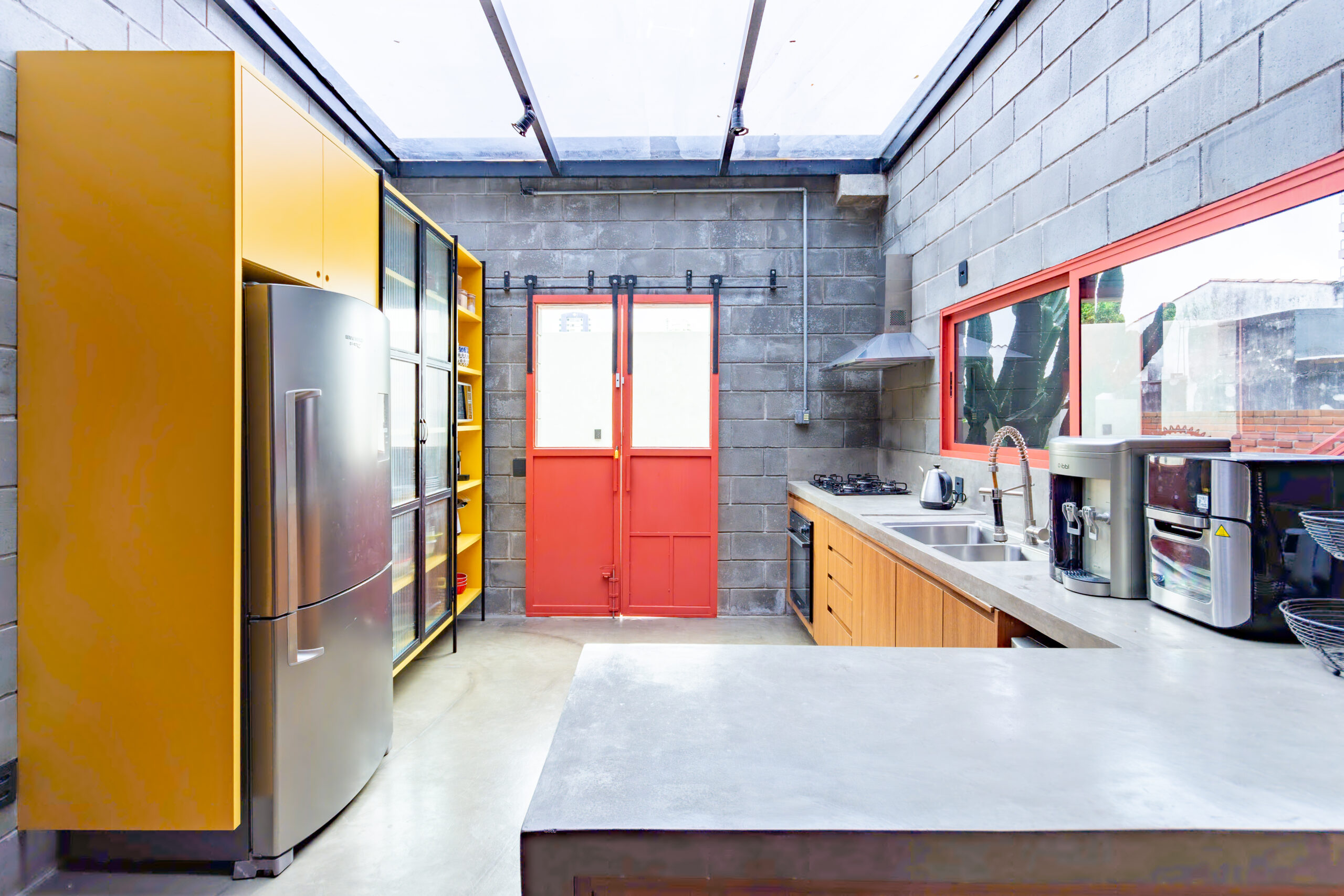 Cozinha integrada com concreto aparente, teto de vidro e móvel amarelo em casa reformada