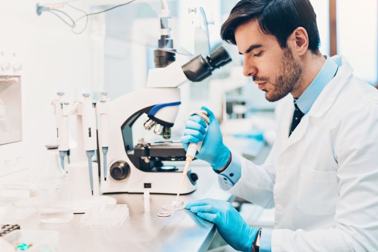 Escolha-Fertilizacao-In-Vitro-Congelamento-Ovulos Médico de pele clara usando jaleco e luvas azuis separando óvulos ao lado de microscópio