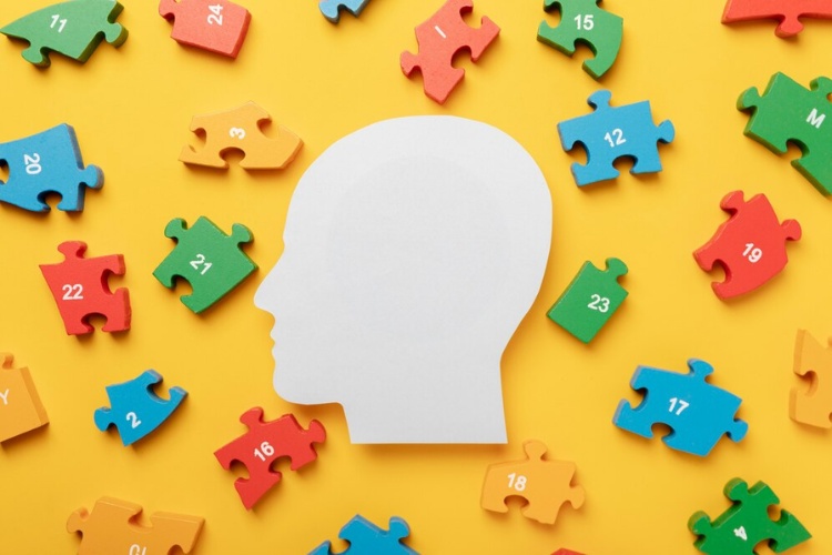 Tdah-E-Autismo-1 Foto de mesa amarela com pças coloridas de quebra-cabeça e papel em formato de cabeça ao centro
