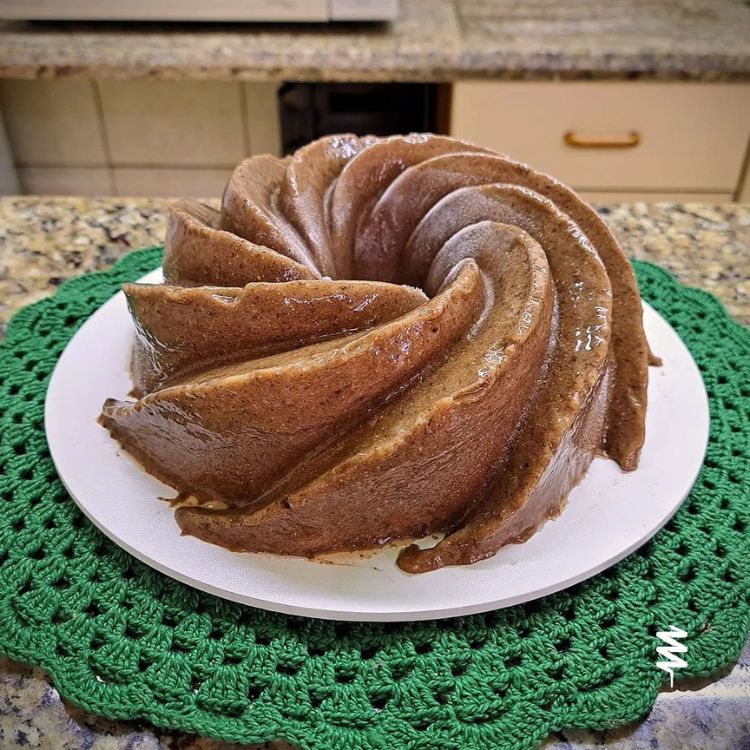 7-3 um pudim desenformado em espiral, amarronzado, sobre prato branco sobre sousplat verde de crochê