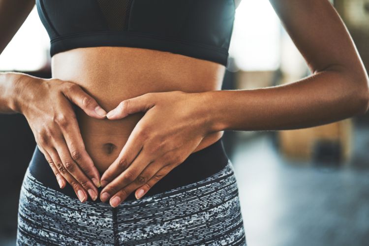 Mounjaro-Remedio-Emagrecer-1 Mulher usando roupas esportivas formando um coração com as mãos sobre o abdômen, sugerindo satisfação com resultados obtidos possivelmente com o tratamento Mounjaro. Imagem simboliza saúde digestiva e bem-estar físico alcançado.