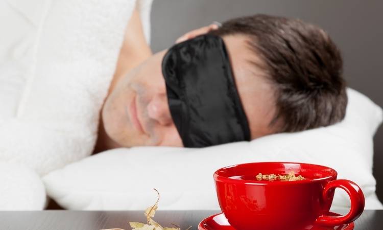 Chás Para Dormir Na Mesa De Cabeceira. Homem dormindo com máscara para os olhos ao lado de xícara vermelha com chá