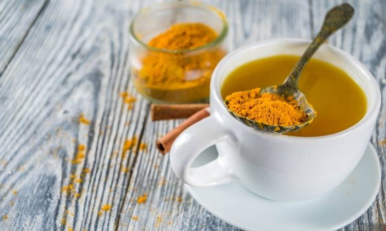 Chá Com Colher De Cúrcuma Em Pó. Xícara branca com chá de cúrcuma