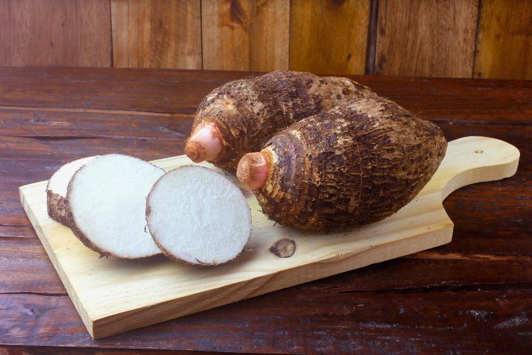 Beneficios-Do-Inhame-Para-A-Saude-1 Inhames inteiros e em rodelas sob uma tábua de madeira que está em uma mesa de madeira rústica