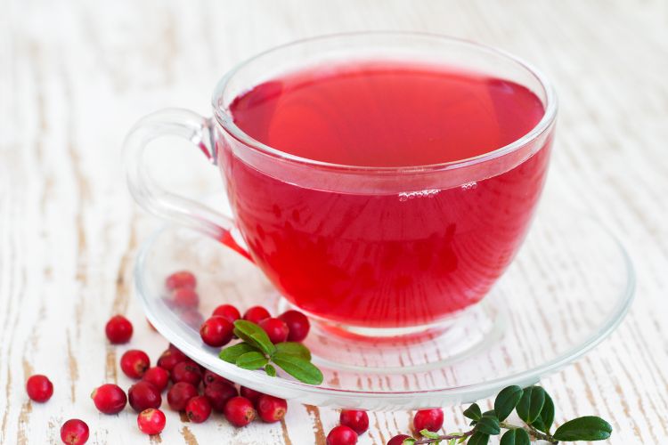 Chas-Infeccao-Urinaria-Cranberry Chá vermelho de cranberry, com frutas ao redor, em xícara e pires transparente