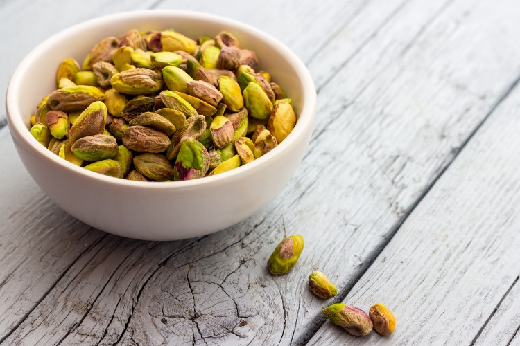 Pistache-Tudo-Sobre pote de cerâmica em superfície de madeira com pistache descascado dentro e espalhados pela superfície