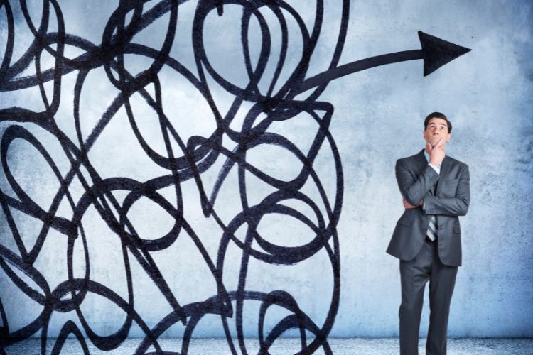 Crise-Em-Oportunidade-5 Homem de terno observa um emaranhado de linhas com uma seta que emerge rumo ao topo, simbolizando solução de problemas e estratégias eficientes. A imagem comunica a ideia de "transforme crise em oportunidade" ao superar desafios com criatividade.