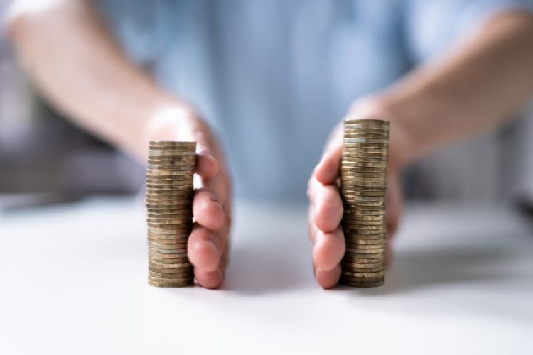 Crise-Em-Oportunidade-12 Duas pilhas de moedas douradas em uma superfície branca, com mãos próximas separando-as cuidadosamente, simbolizando gestão financeira, controle de gastos e estratégias para organização de recursos durante momentos de planejamento ou crise econômica. Fundo levemente desfocado.