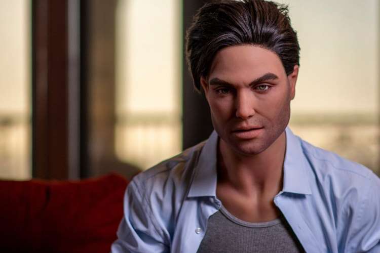 Boneco-Reborn-Adulto-Homem Boneco homem realista, adulto reborn, usando camisa social sentado em sofá vermelho com fundo desfocado.