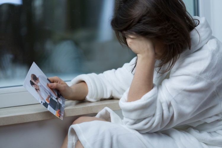 Sonhar-Com-Ex-Namorado-3 Mulher de pele clara usando roupão, com a mão no rosto, enquanto segura foto de casal heterossexual