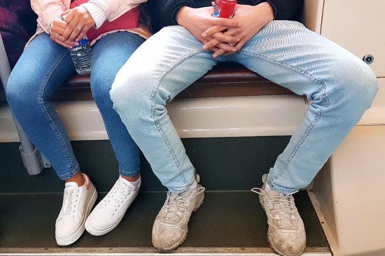 Manspreading-2 Homem de calça jeans com pernas abertas em assento, deixando mulher também de calça jeans sem espaço