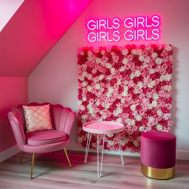Letreiro-Neon-12 Um quarto rosa. Uma parede com flores artificiais cor-de-rosa e brancas. À esquerda, uma poltrona rosa aveludada, uma mesinha rosa e à direita um pufe rosa escuro. Acima, um neon rosa diz "GIRLS GIRLS GIRLS GIRLS GIRLS".