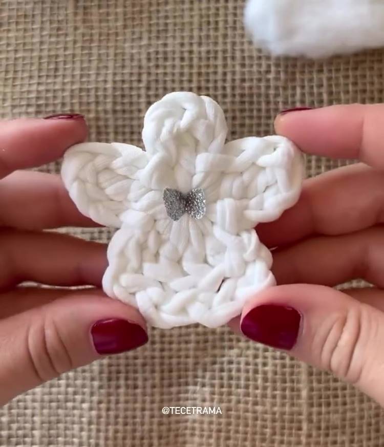 Ggg-1-Frame-At-1M29S Mãos com unhas vermelhas segurando Anjo de crochê de Natal branco com laço prateado