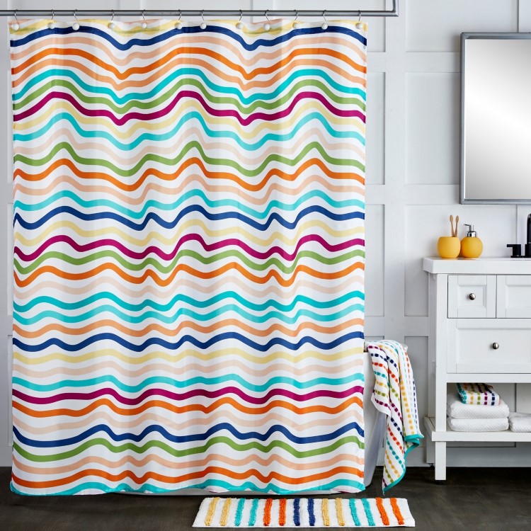 Casa-Decorada-Lgbtqia-1 Banheiro iluminado com cortina de chuveiro decorada com listras onduladas multicoloridas, combinando com tapete listrado colorido. Pia branca com espelho retangular, acessórios amarelos e toalhas dobradas. Design alegre e funcional com detalhes organizados.