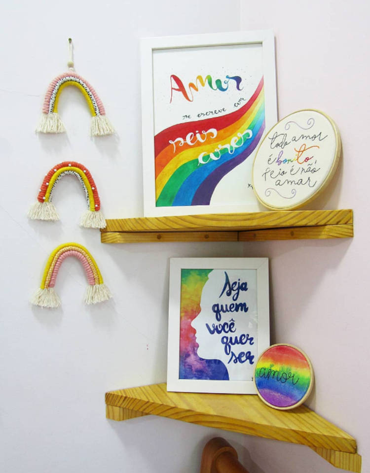 Orgulho Da Bandeira Lgbtqia+. Cantinho com as cores da bandeira LGBTQIA+ em quadro escrito "amor se escreve em seis cores", bastidor com frase "todo amor é bonito, feio é não amar", quadro d emoldura branca com frase "seja quem você quer ser", bastidor colorido escrito "amor" e 3 arco-íris de macramê pendurados