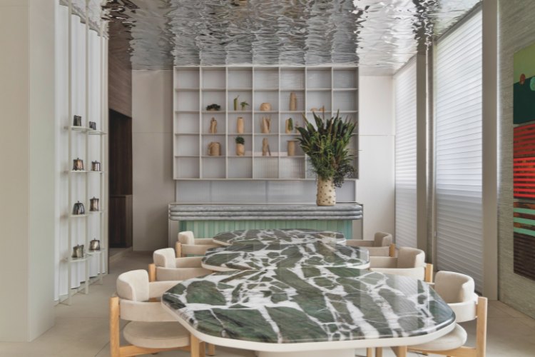 Casacor-Sao-Paulo-2025-3 Mesa de mármore com cadeiras claras, prateleiras e teto metálico