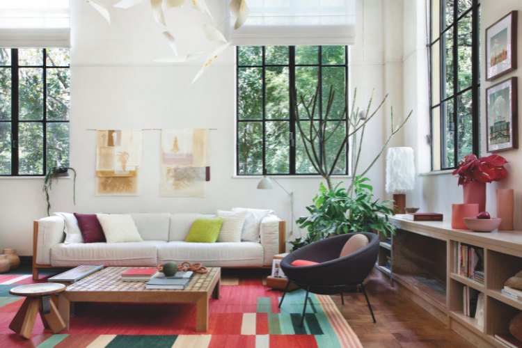 Casacor-Sao-Paulo-2025-5 Sala com tapete colorido, grandes janelas, sofá claro, poltrona roxa, mesa de centro e mais